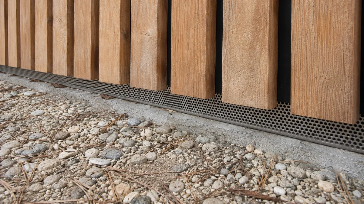 Entrée d'air en pied de façade d'un bardage à claire-voie, fermée par une grille anti-rongeurs