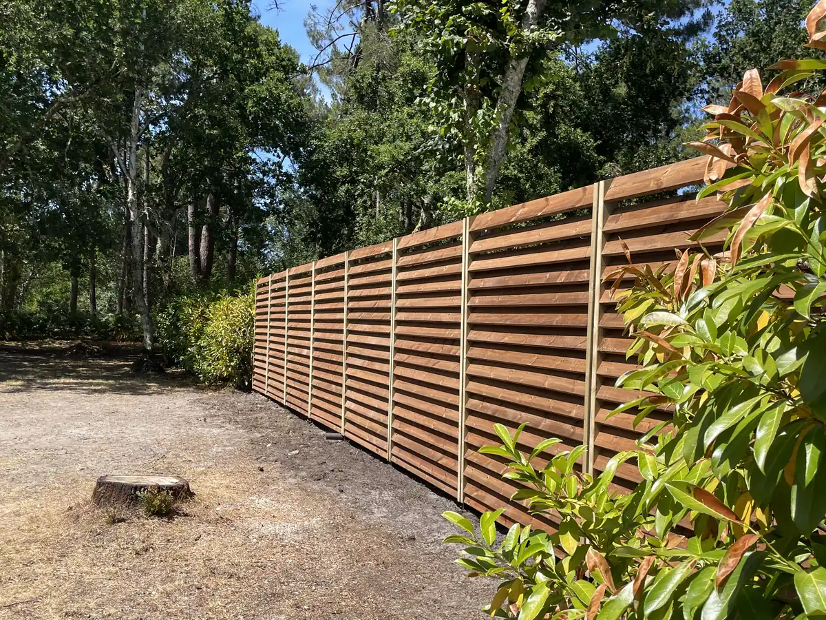 Clôture bois à lames horizontales vue en enfilade le long d’une parcelle boisée