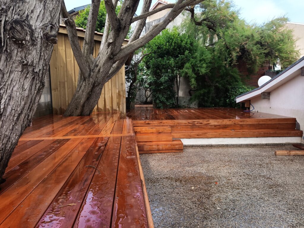 Terrasse en bois exotique sur deux niveaux, découpée autour d'un arbre, lames encore humides