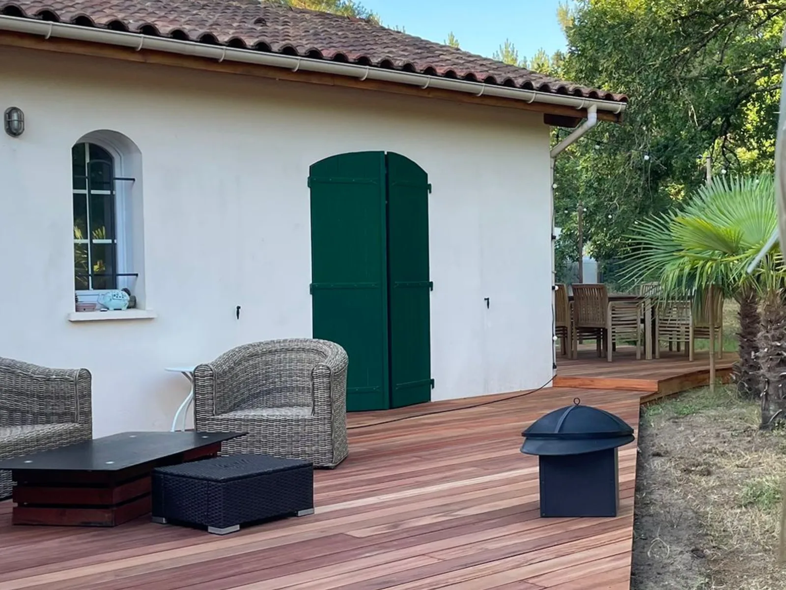 Terrasse en bois exotique devant une maison girondine aux volets verts