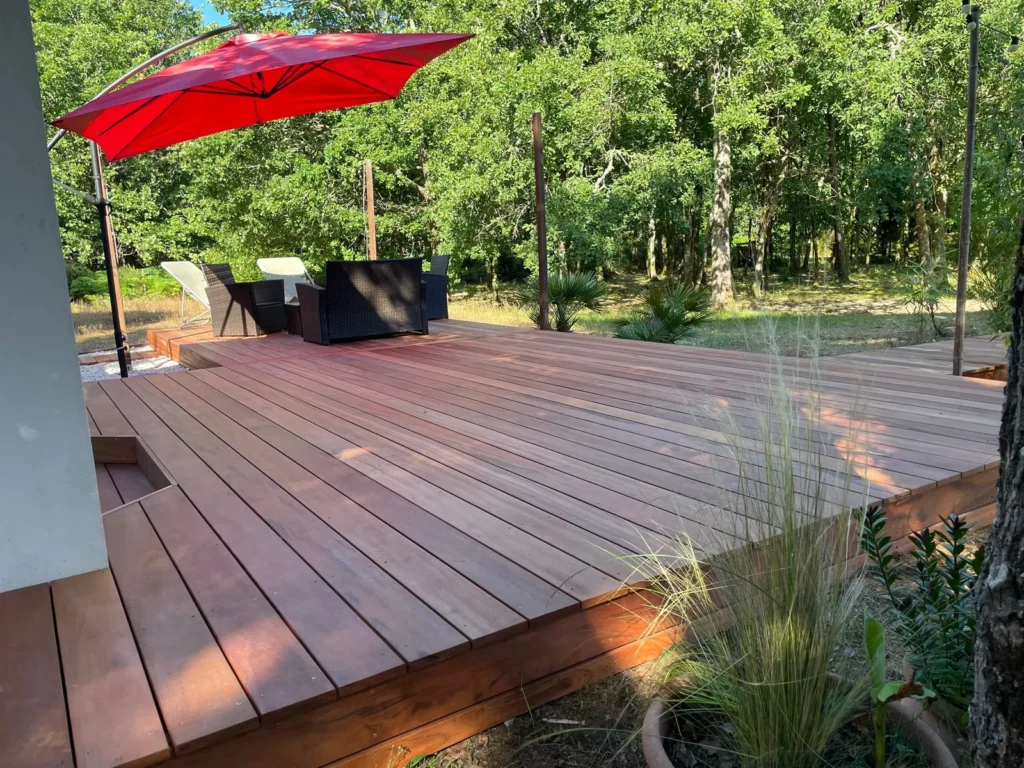 Terrasse en bois exotique muiracatiara, parasol rouge et pins en arrière-plan