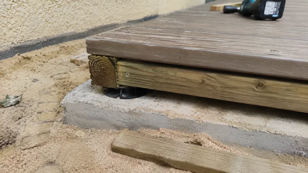 Tranche d'une terrasse en bois en cours de pose sur dalle béton : lame, lambourde et cale