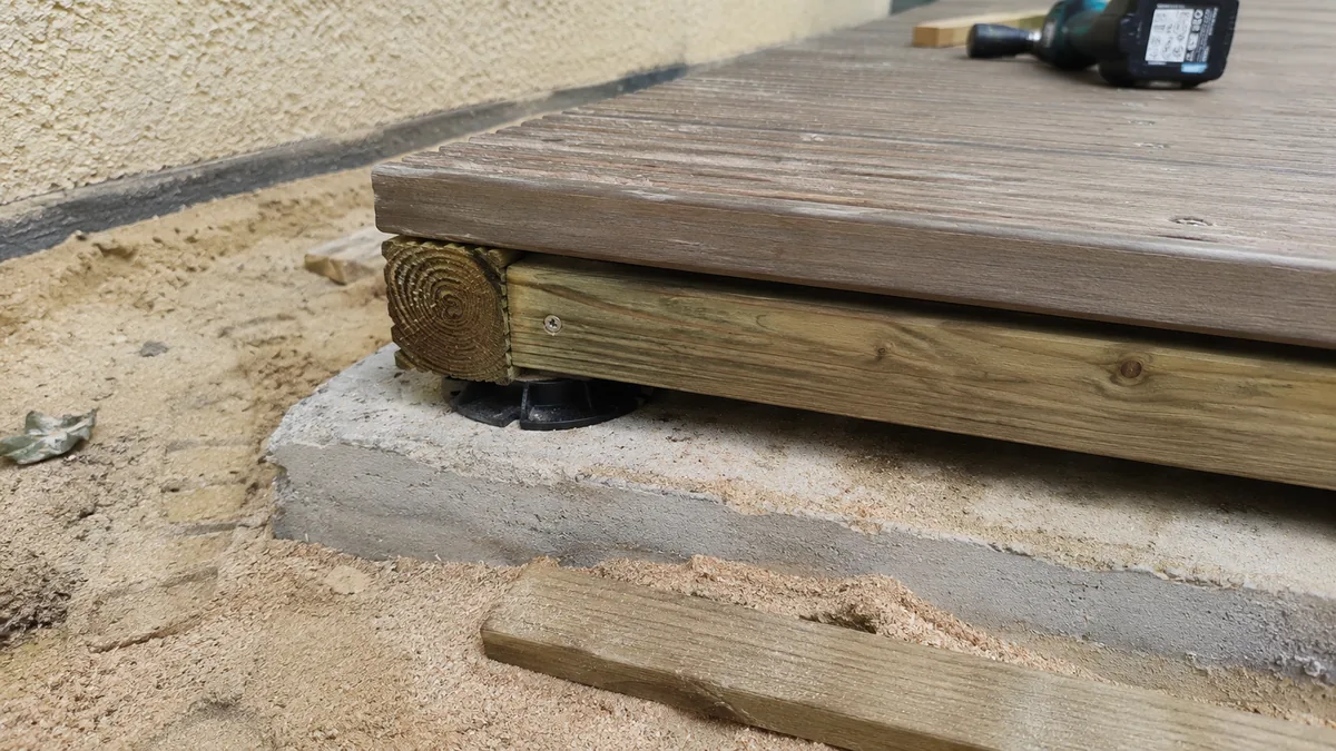 Tranche d'une terrasse en bois en cours de pose sur dalle béton : lame, lambourde et cale