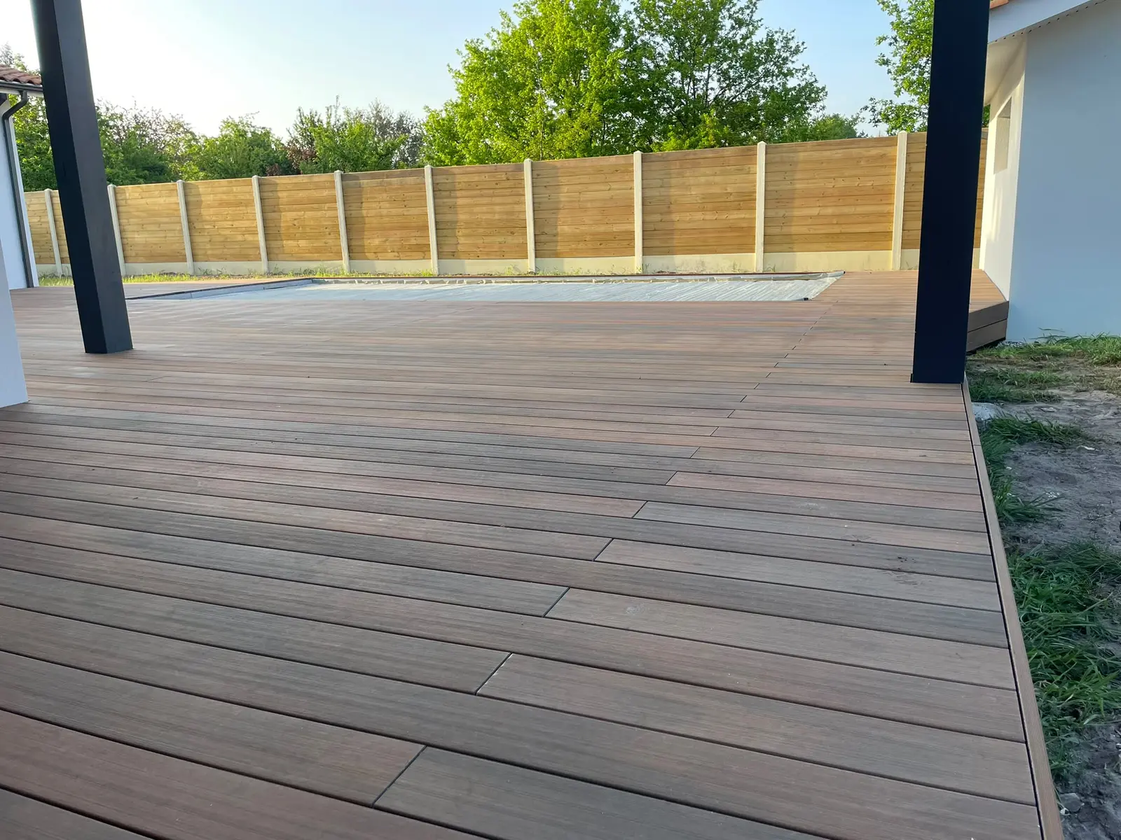 Terrasse en bois composite de 90 m² posée par Sol et Bois autour d’un bassin, lames brunes et clôture bois